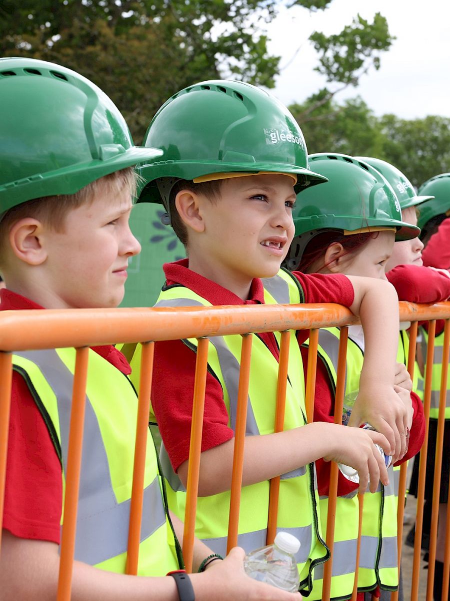 School children in PPE at building site.